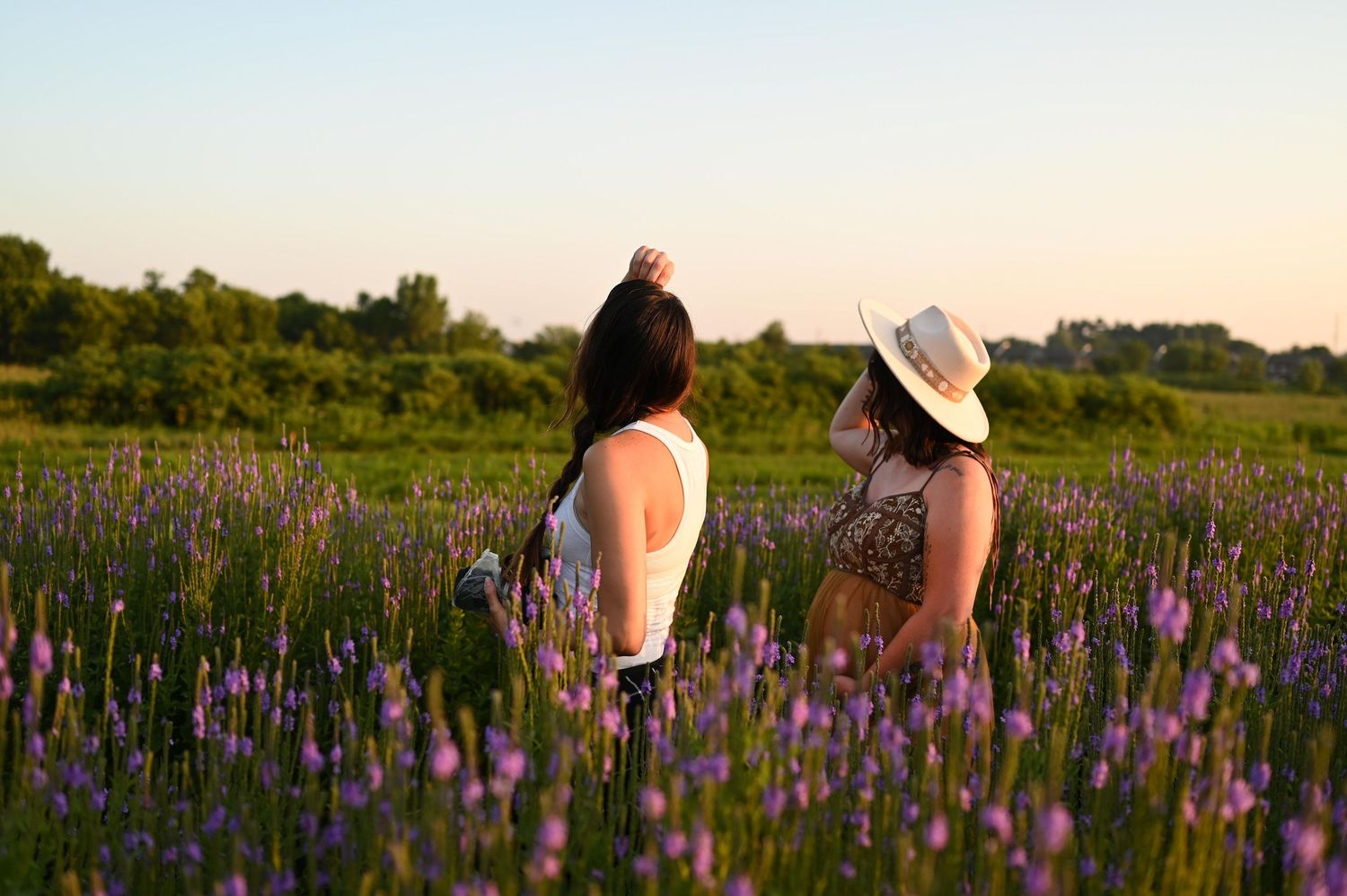 A couple walks hand in hand through a vibrant purple wildflower meadow during golden hour.