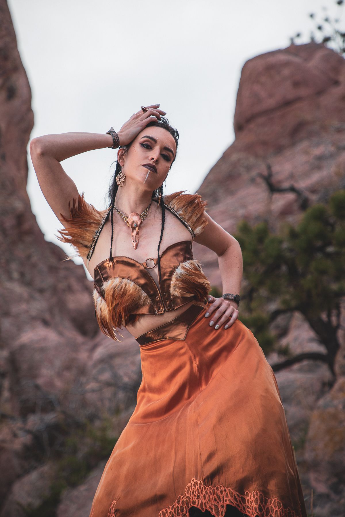 Desert-inspired fashion pose in flowing rust-colored dress against red rock landscape.