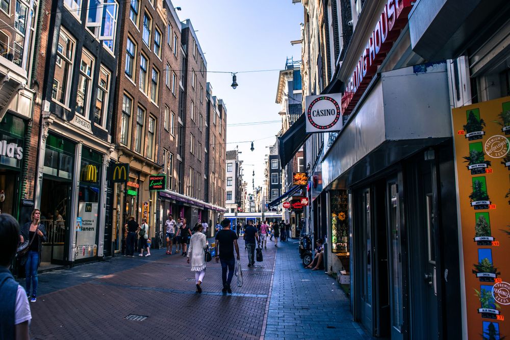 Busy shopping street in Amsterdam's historic center with traditional Dutch buildings.