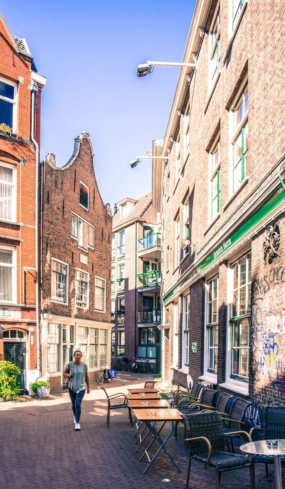 Narrow cobblestone street in Amsterdam with classic Dutch architecture and outdoor cafe seating.