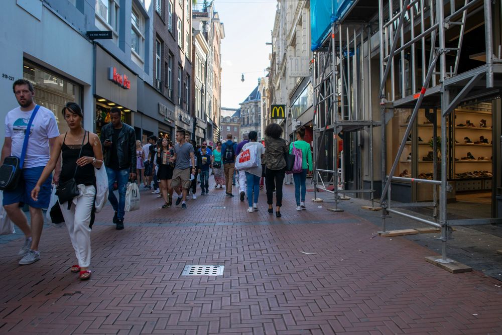 Pedestrians walking on a brick shopping street lined with stores in Amsterdam's city center.