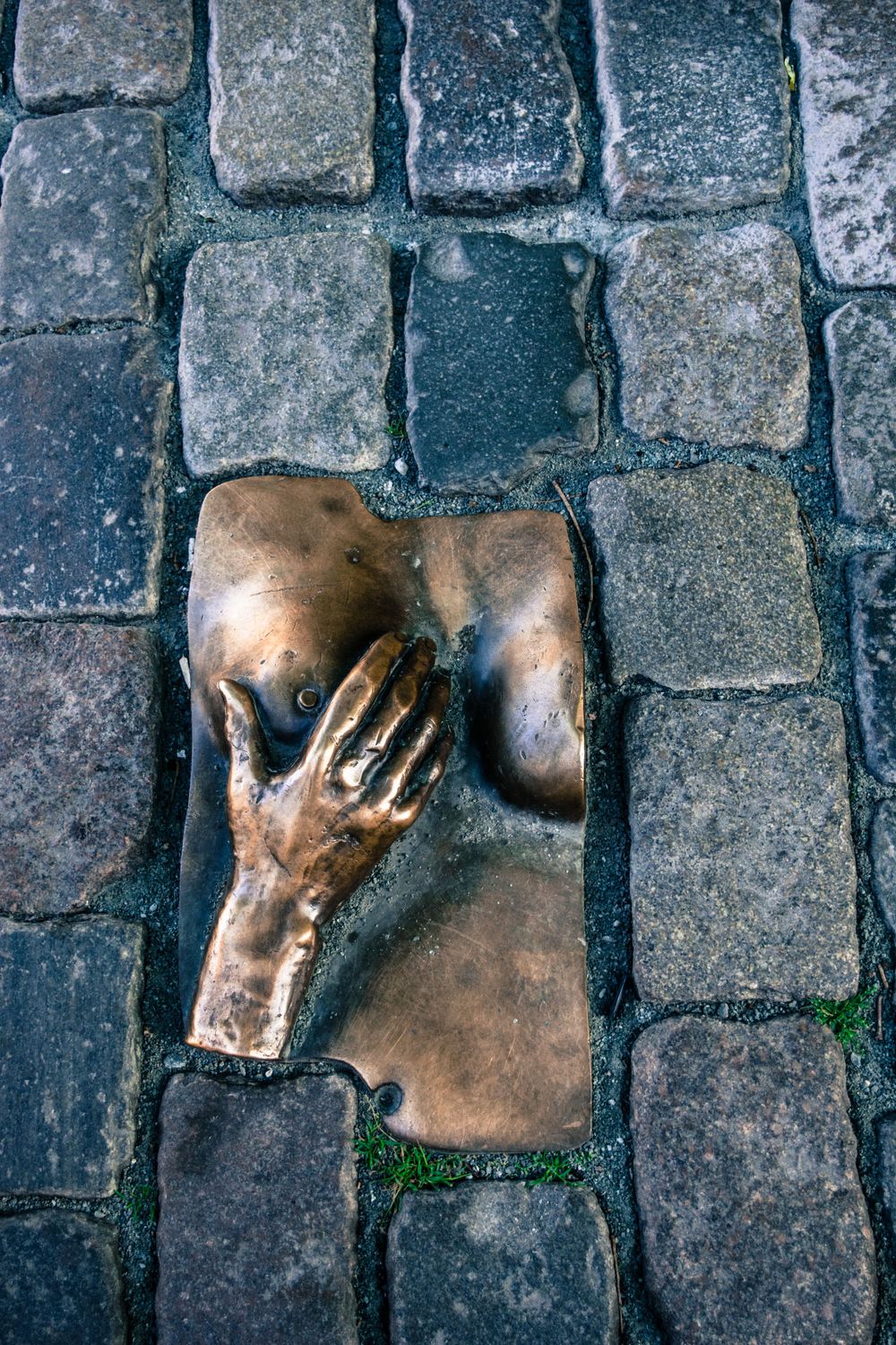 Bronze art installation of a hand embedded in cobblestone street pavement.