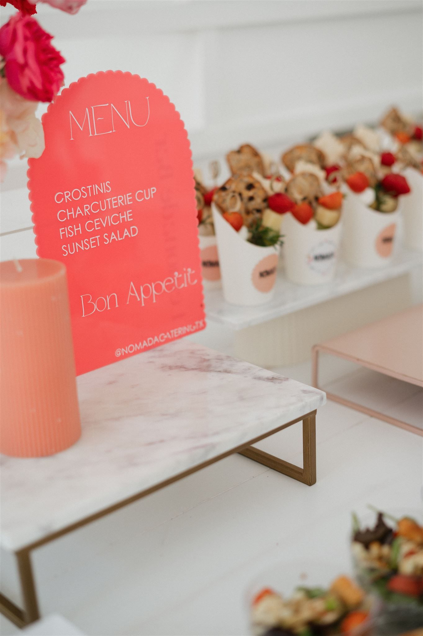 Pink menu card and appetizer bites displayed on a marble table at an elegant event setup.