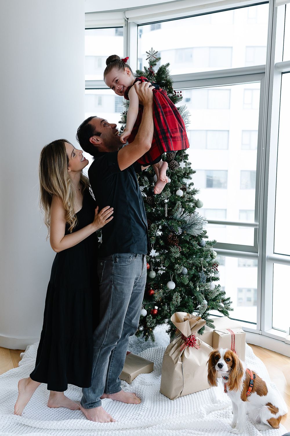 A family shares a joyful moment by their Christmas tree with their Cavalier King Charles Spaniel.