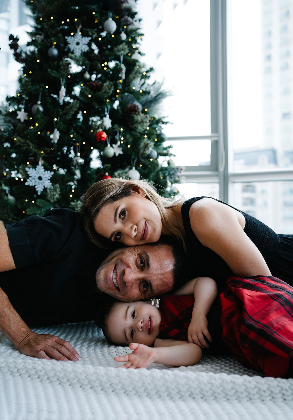 A family lying together on a white carpet in front of their Christmas tree.