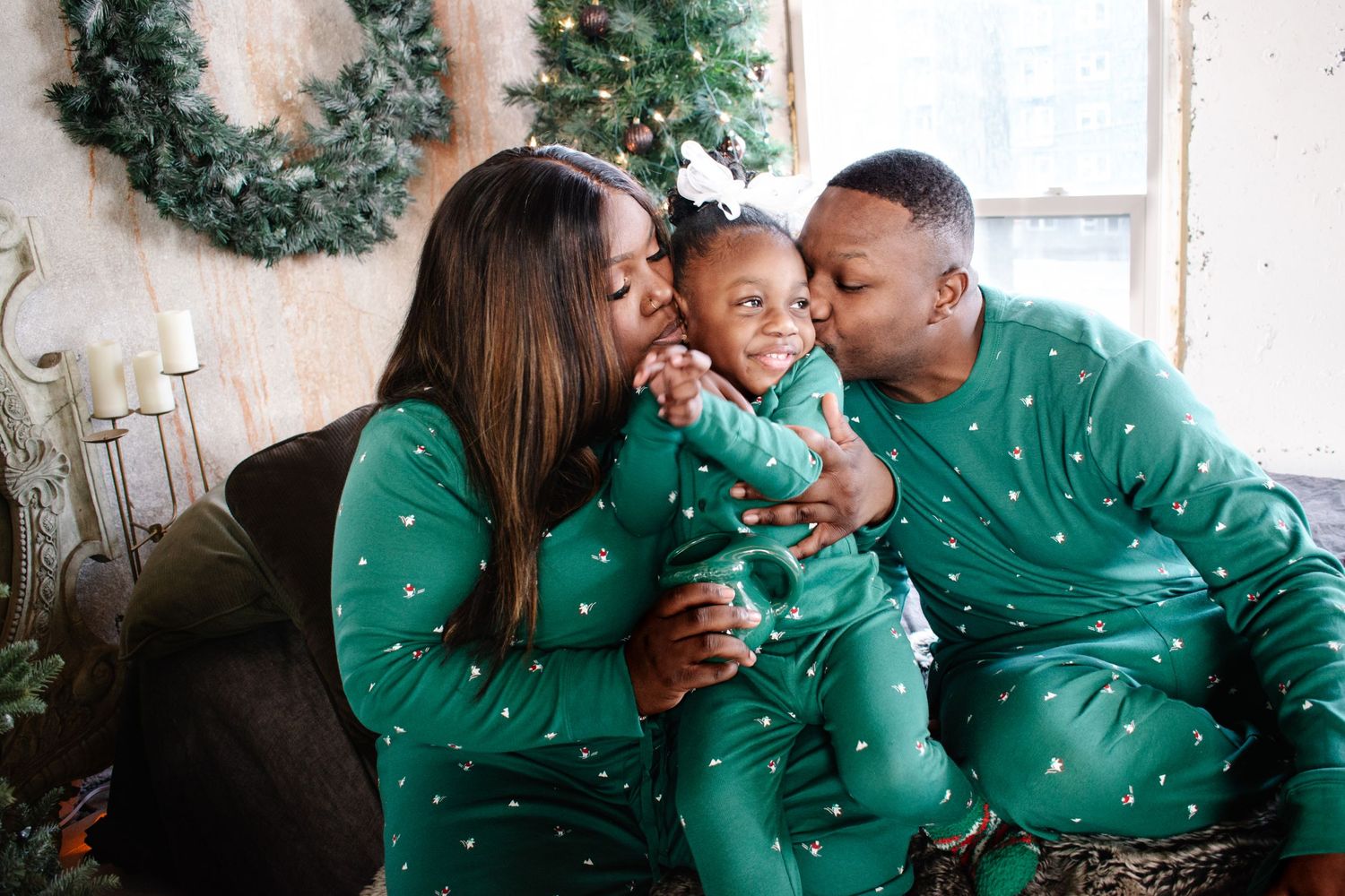 A joyful holiday family session featuring parents and their baby in festive matching green pajamas sharing smiles by a Christmas tree