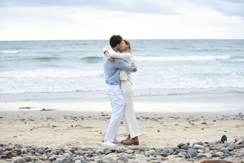 A loving embrace on a sandy beach with ocean waves in the background.