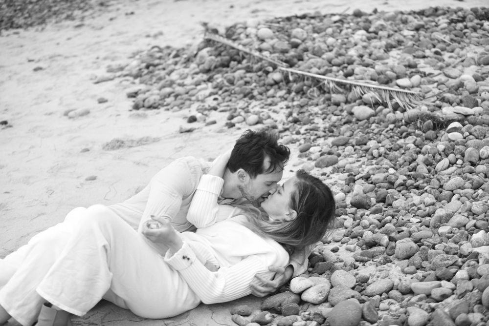A couple lying on a rocky beach sharing tender moments during a photoshoot.