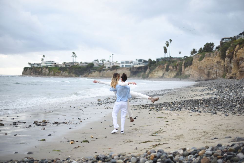 A panoramic view of a rocky beach with cliffs and two people walking in the distance.