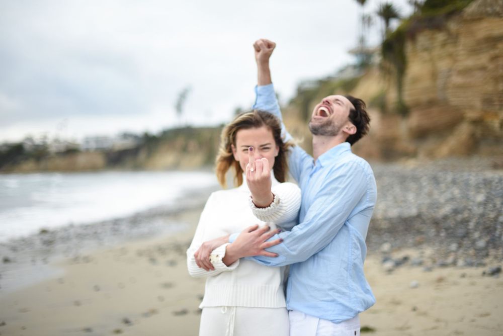 A playful candid moment captured on a rocky beach with cliffs in the background.