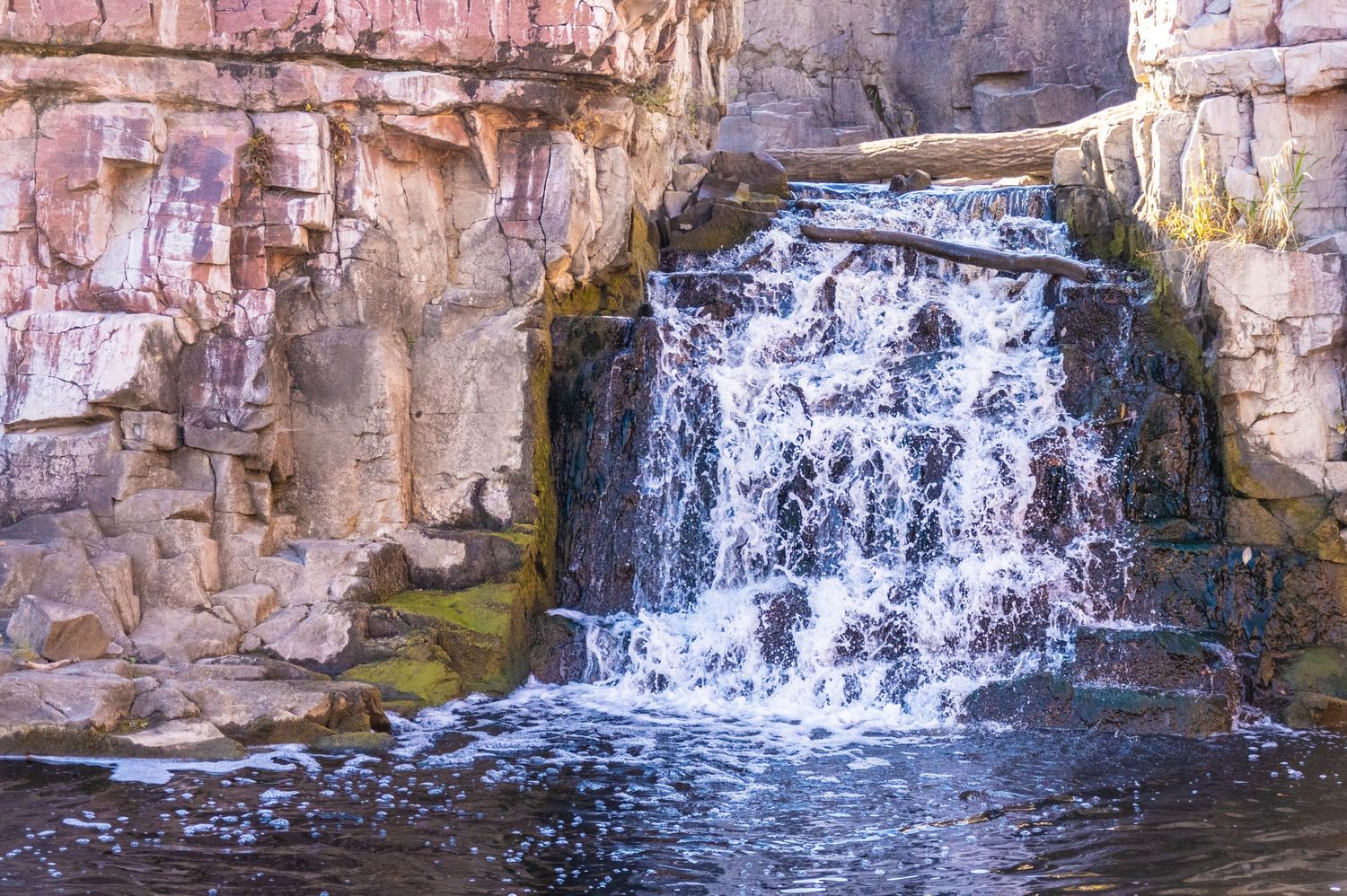 Water cascades down pink limestone cliffs into a tranquil pool below.