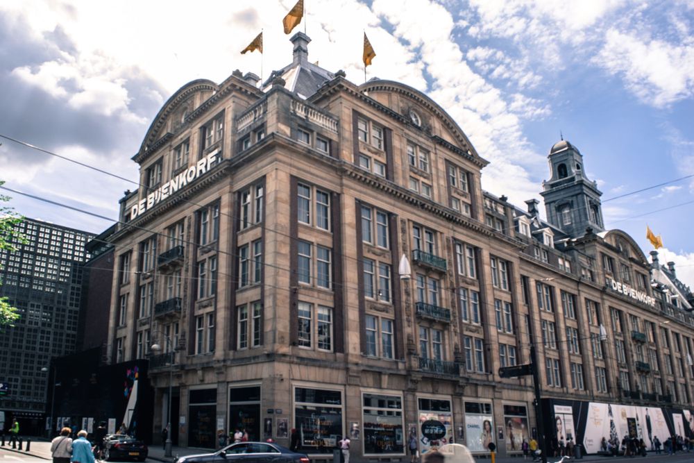 Grand historic department store building with baroque architecture and flags in Amsterdam city center.