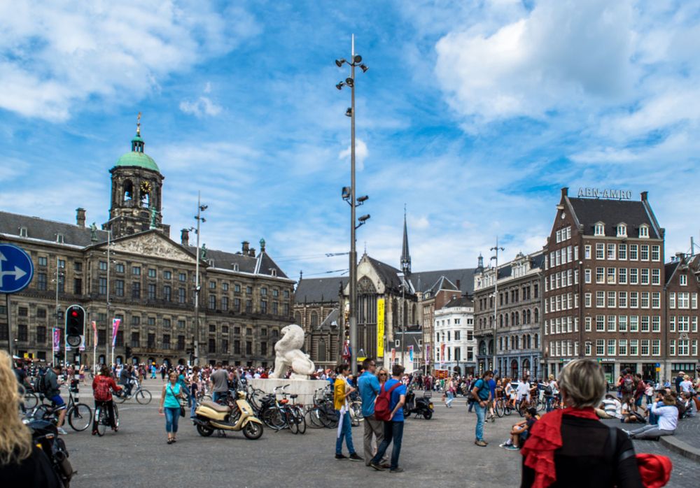 Busy Dam Square in Amsterdam with Royal Palace and historic architecture under blue skies.