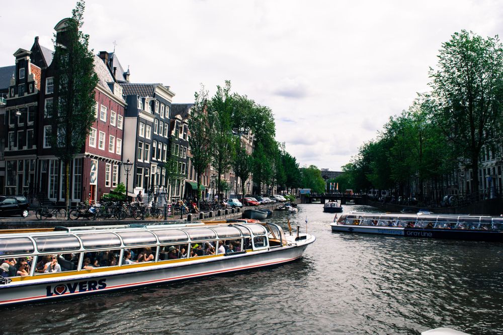 Tourist boats navigate Amsterdam's scenic canal lined with traditional Dutch townhouses.