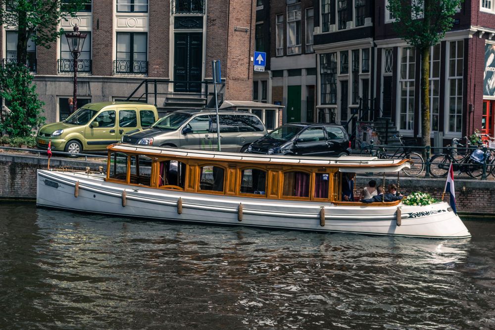 Traditional wooden tour boat cruising through Amsterdam canal with historic buildings in background.
