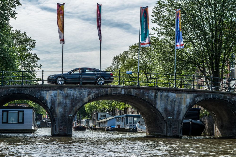Stone arch bridge with colorful banners spanning canal in Amsterdam with boats below.