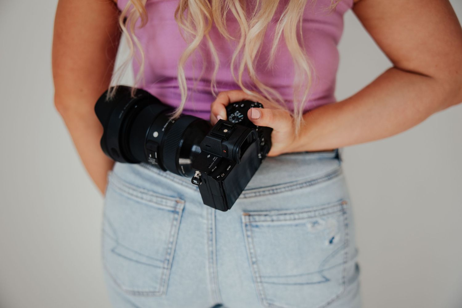 Close up of a Canon camera being held at hip level with light wash denim jeans in frame.