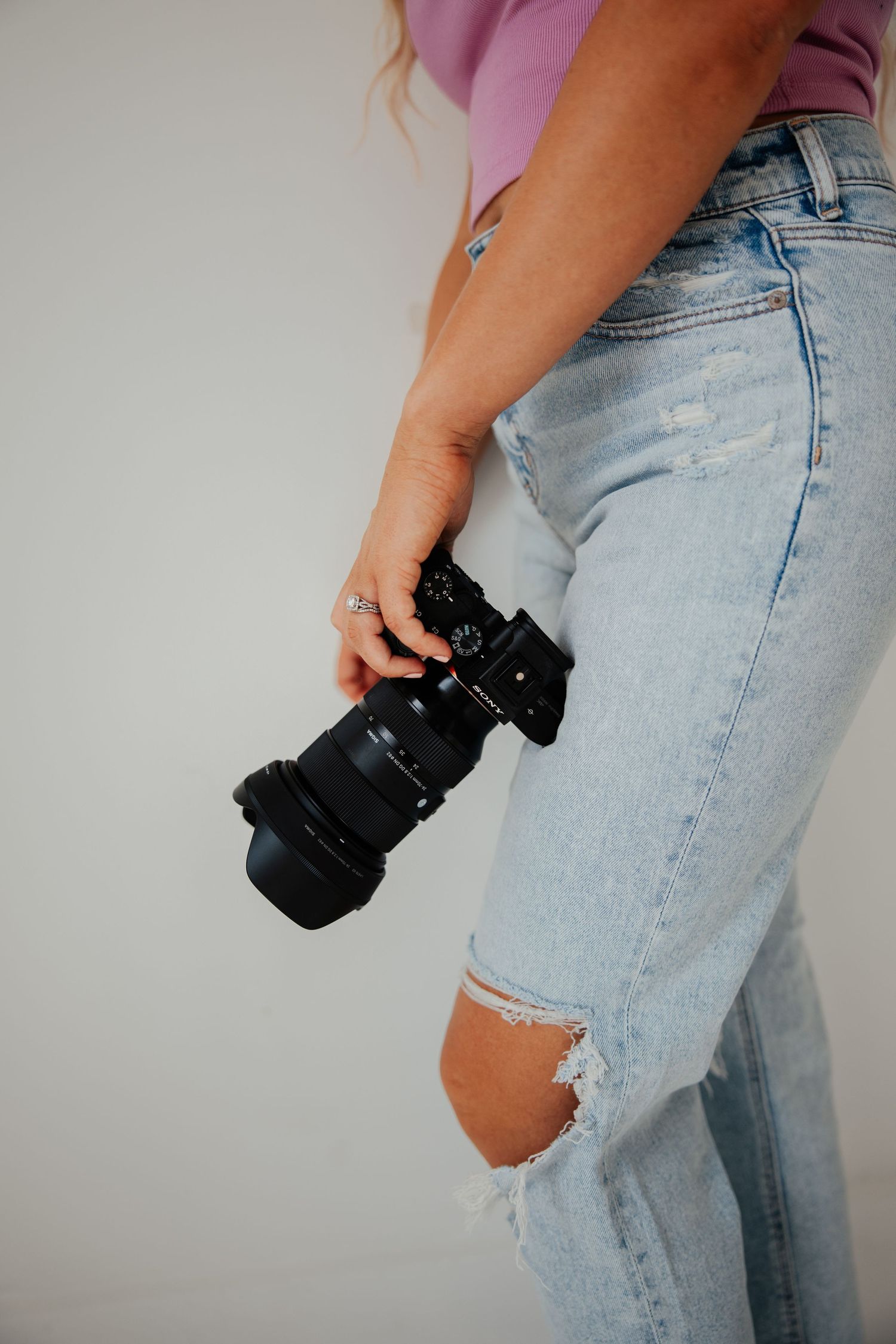 Detail shot of photographer holding a mirrorless Sony camera wearing ripped light wash jeans.