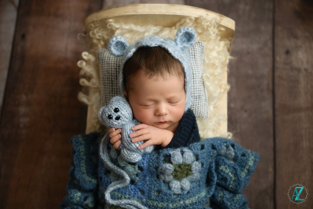 Sleeping newborn in blue knit outfit with bear ears in vintage wooden prop.