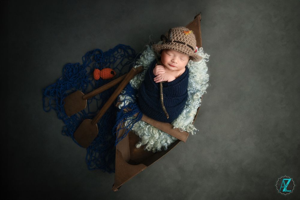 Sleeping baby posed in wooden boat with blue fabric and knit accessories.