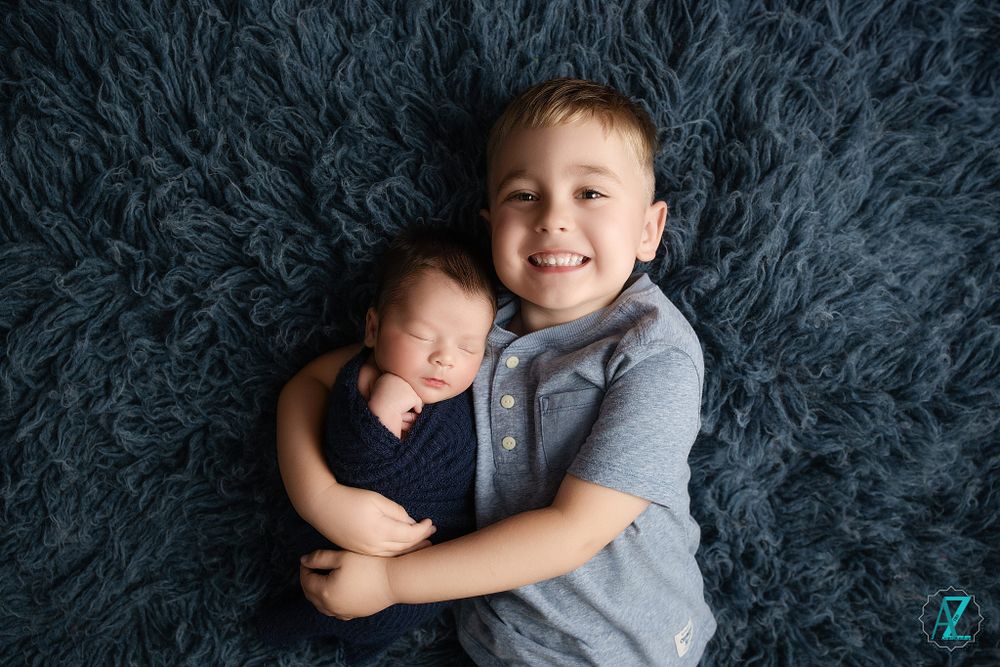 Two young siblings sharing a tender moment while lying on a plush gray rug.