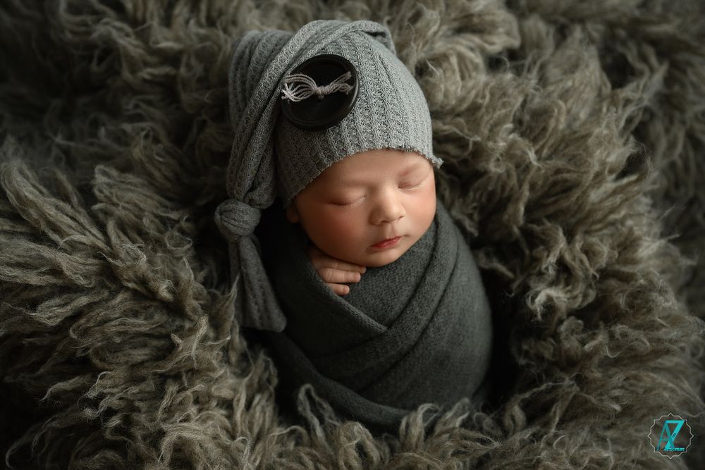 Newborn baby wrapped in gray swaddle wearing knit hat on furry backdrop.