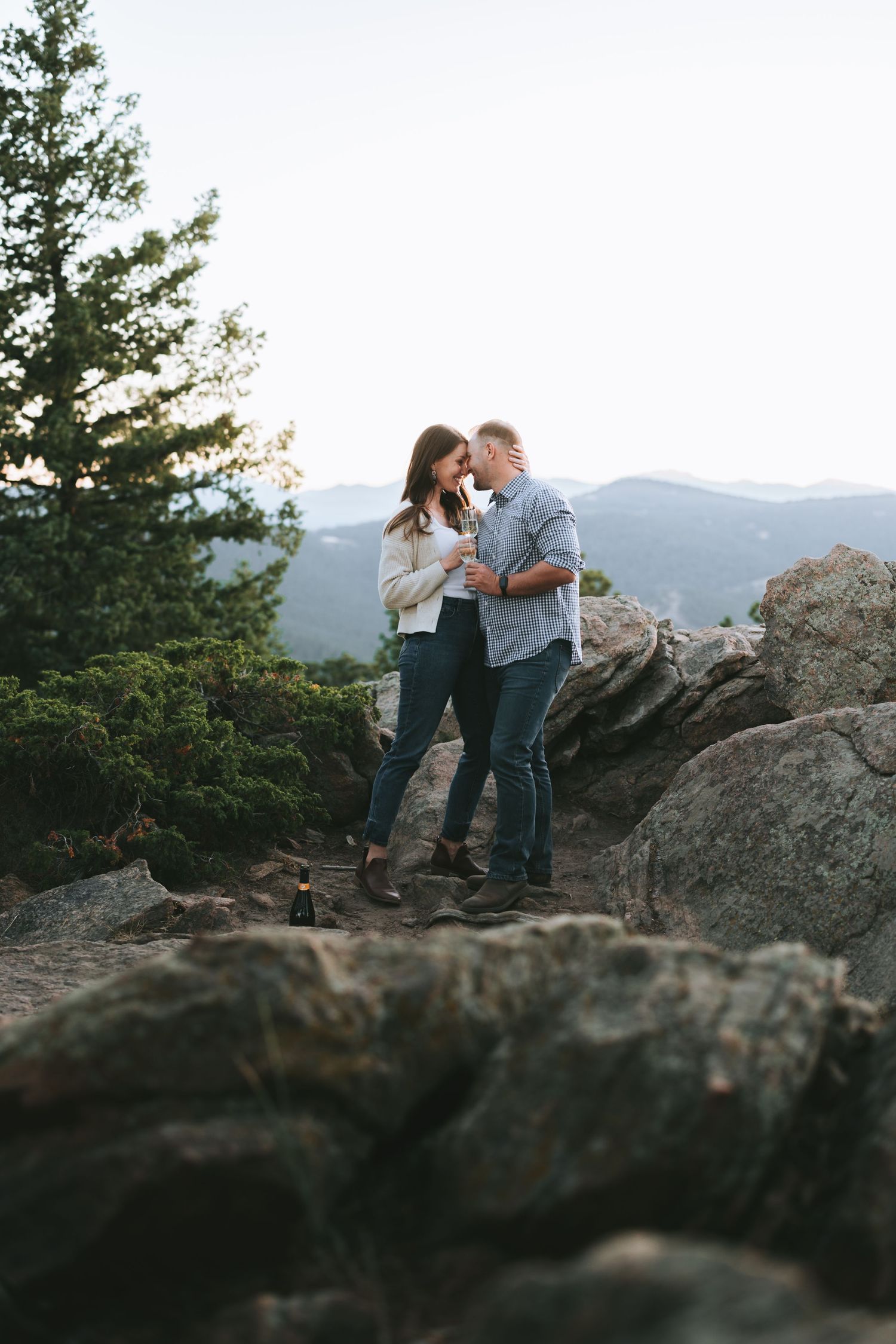 A couple shares an intimate moment while standing on rocky mountain terrain at dusk.