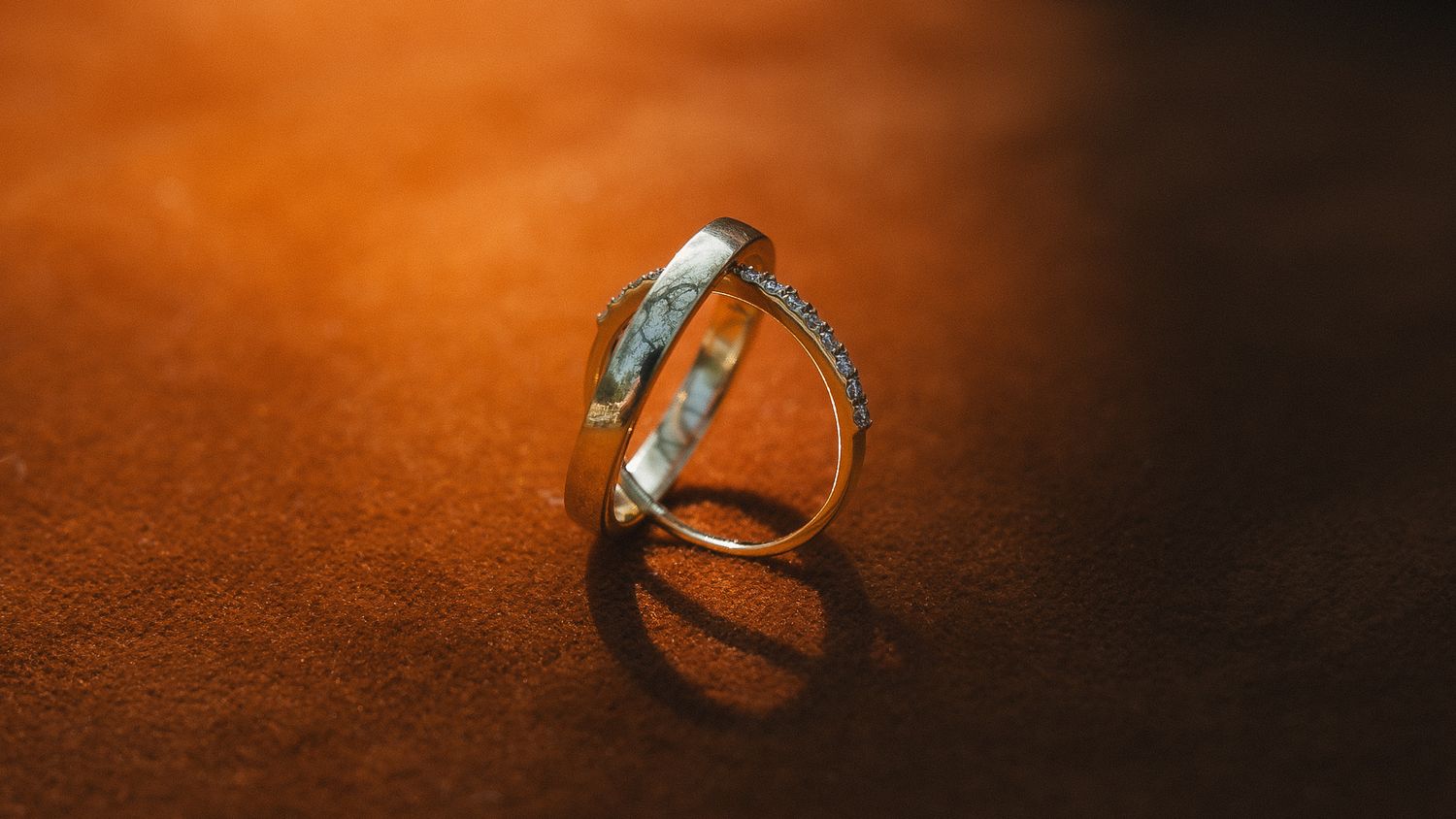 Two silver wedding rings casting shadows on a textured orange-brown surface in dramatic lighting.
