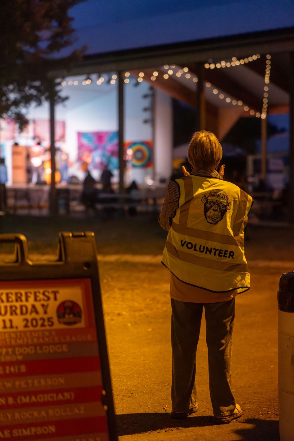 Event volunteers stand at dusk against a backdrop of twinkling lights and festival signage.