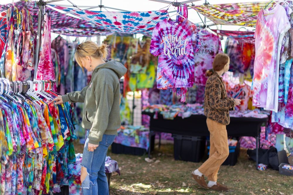 Colorful tie-dye tapestries and clothing displayed at an outdoor market or festival booth.