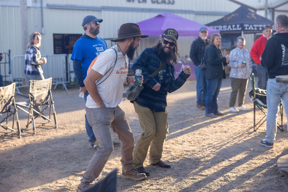 Festival attendees walk along a dusty path between vendor stalls and tents at an outdoor event.