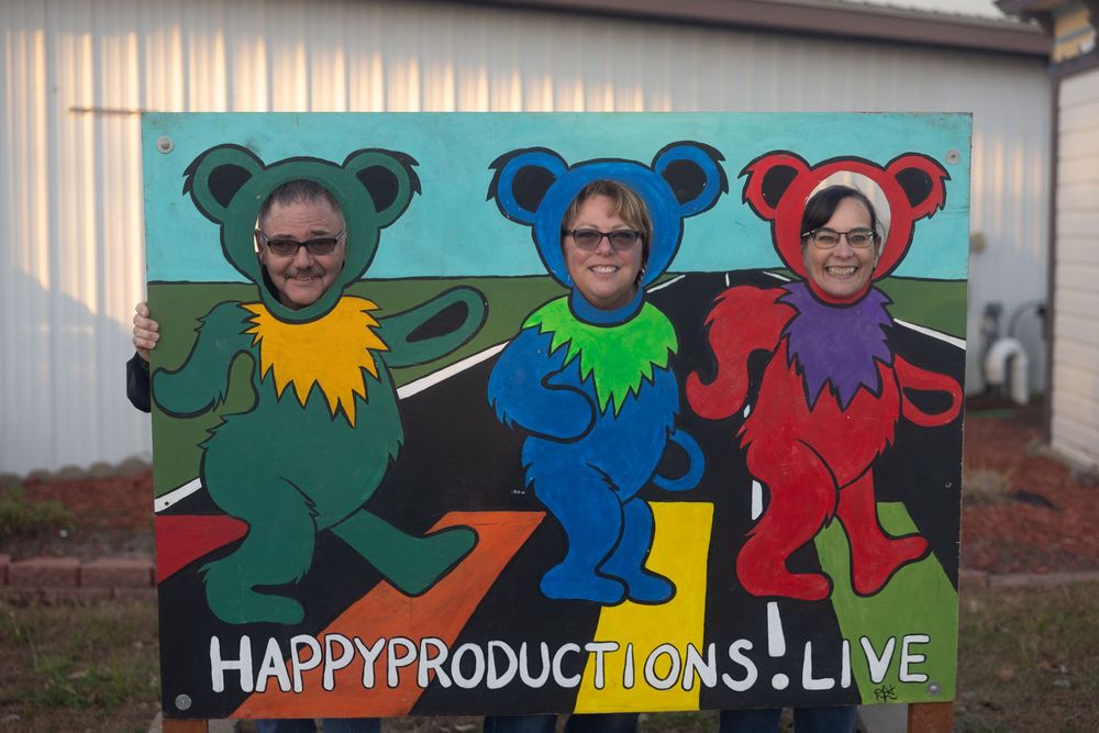 Colorful cartoon-style signage displays 'Happy Productions Live' with vibrant character designs.