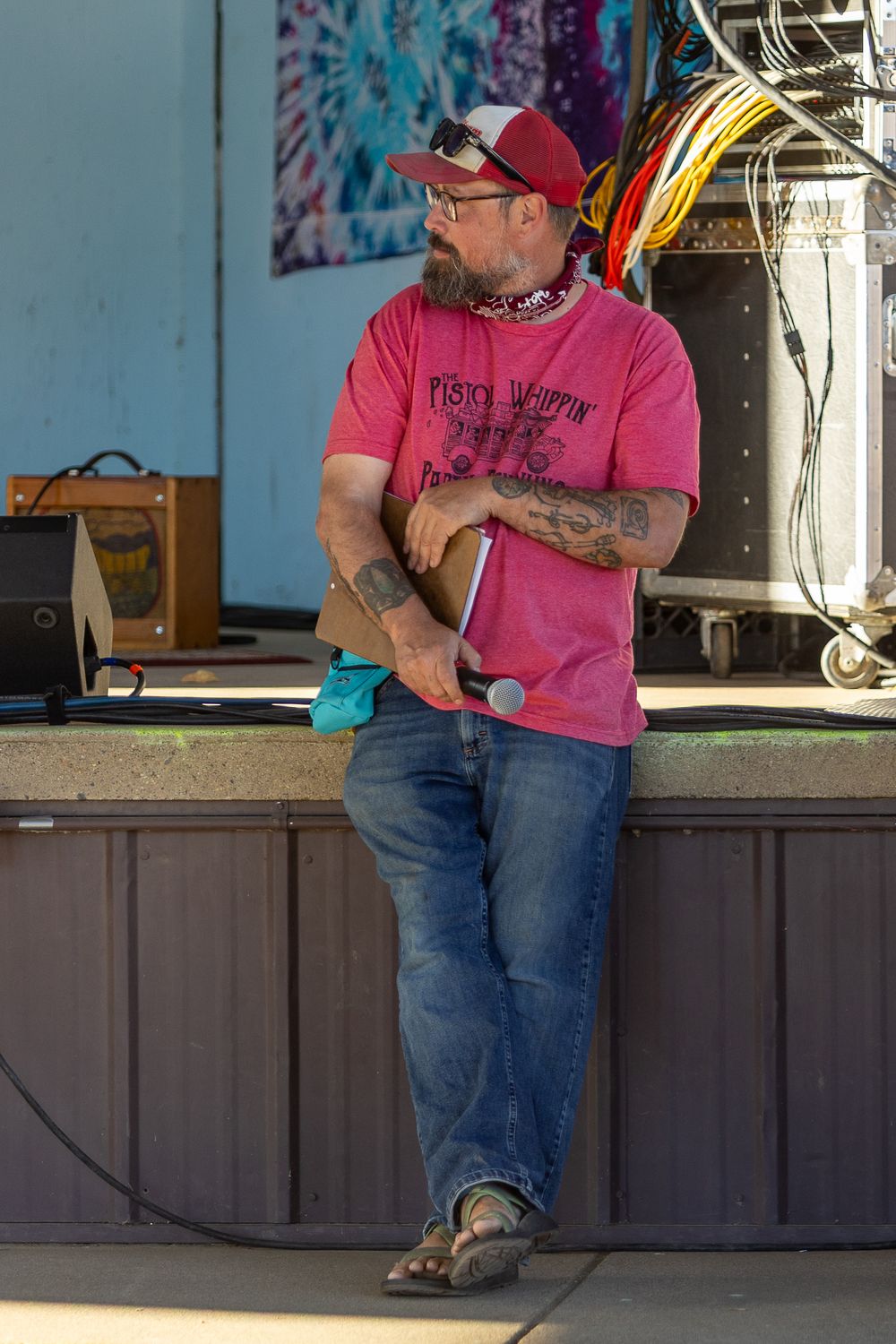 Person in pink shirt and jeans sits on edge of wooden stage during outdoor event.