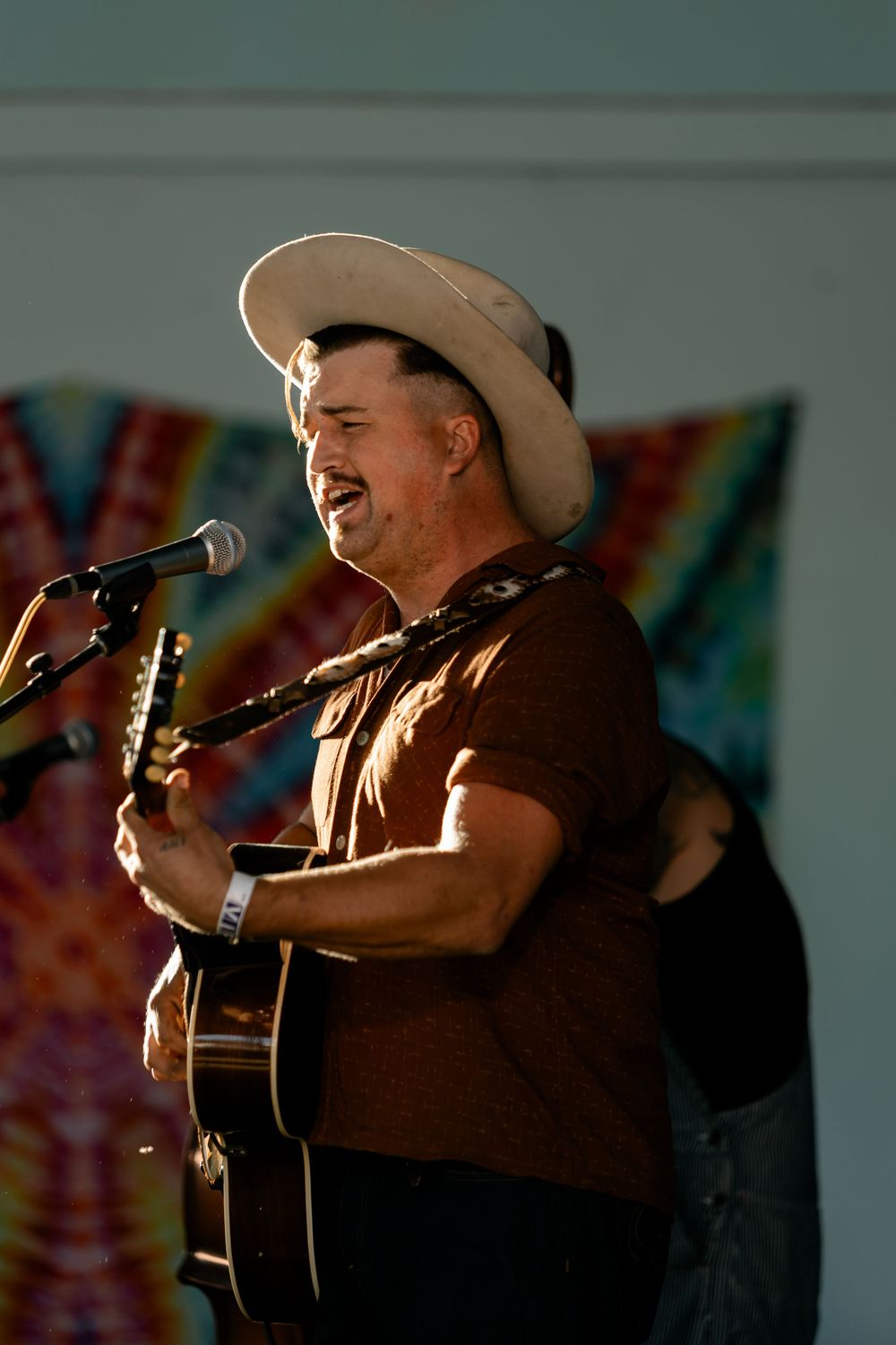 Musician performs with acoustic guitar under stage lighting against colorful backdrop.