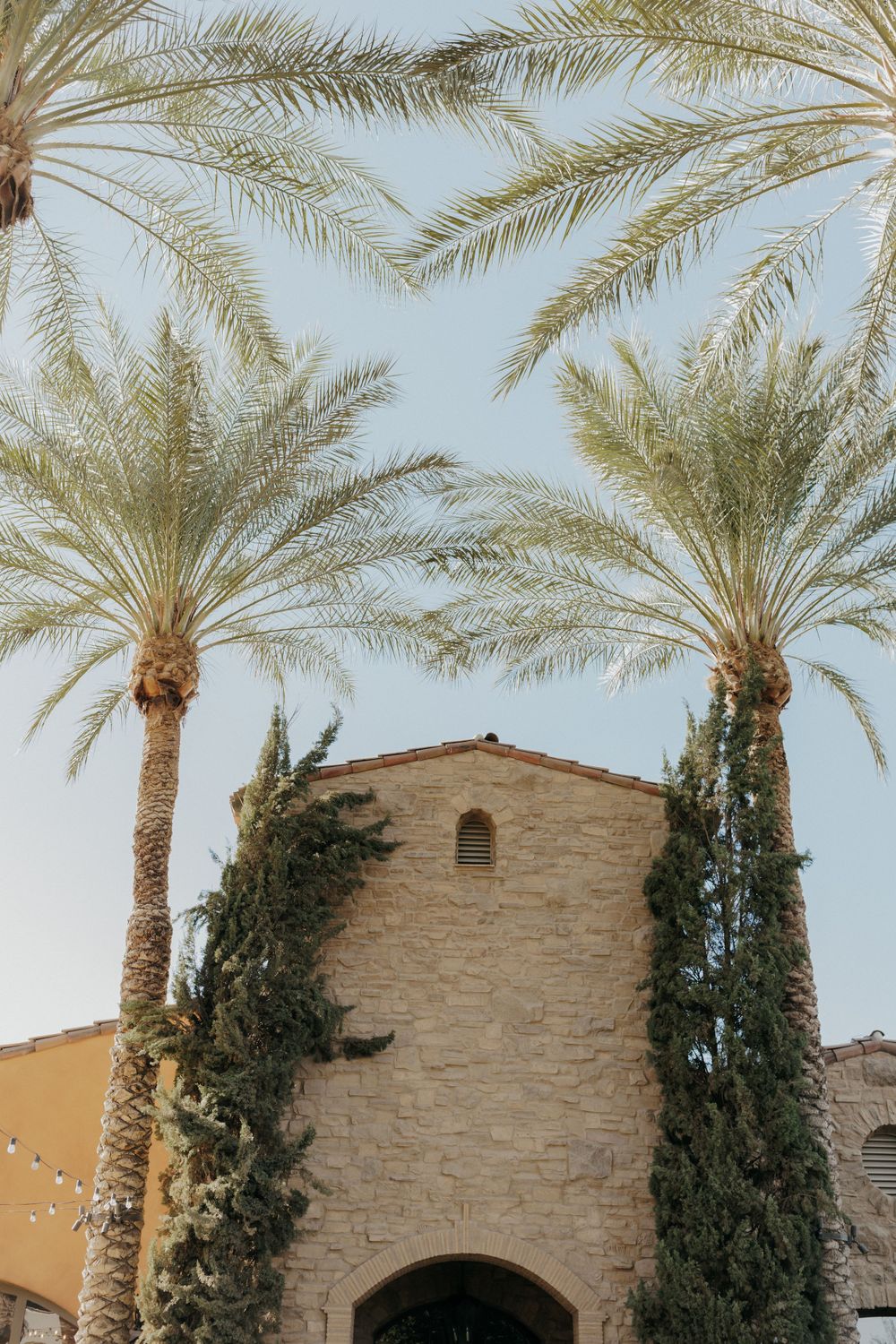 Mediterranean style stone building with tall palm trees framing the entrance against a blue sky.