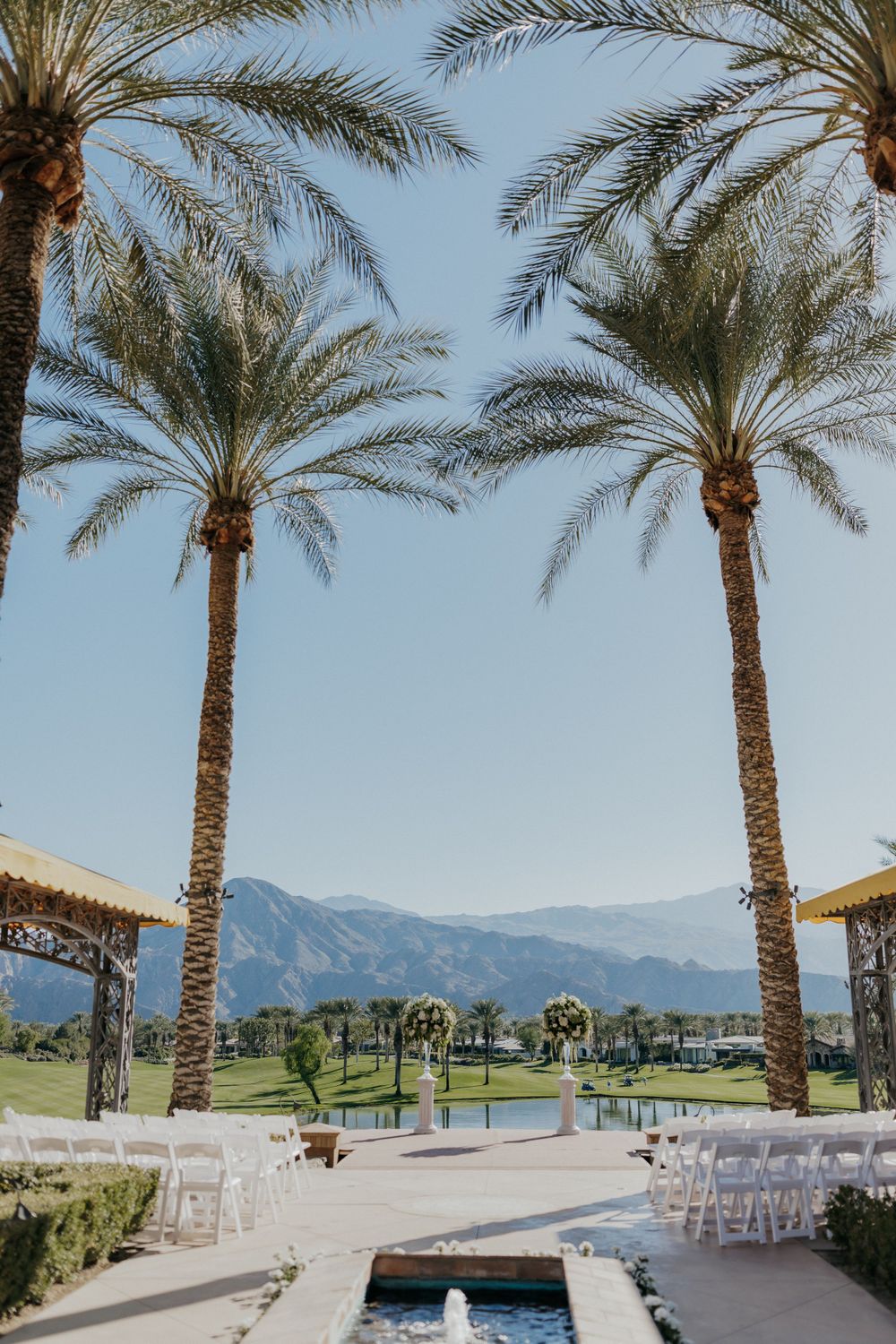 Outdoor wedding venue with palm trees framing mountains and a lake view.