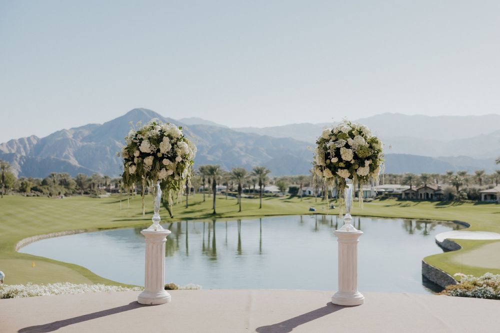 Wedding ceremony setup with floral pillars overlooking a mountain landscape and pond.