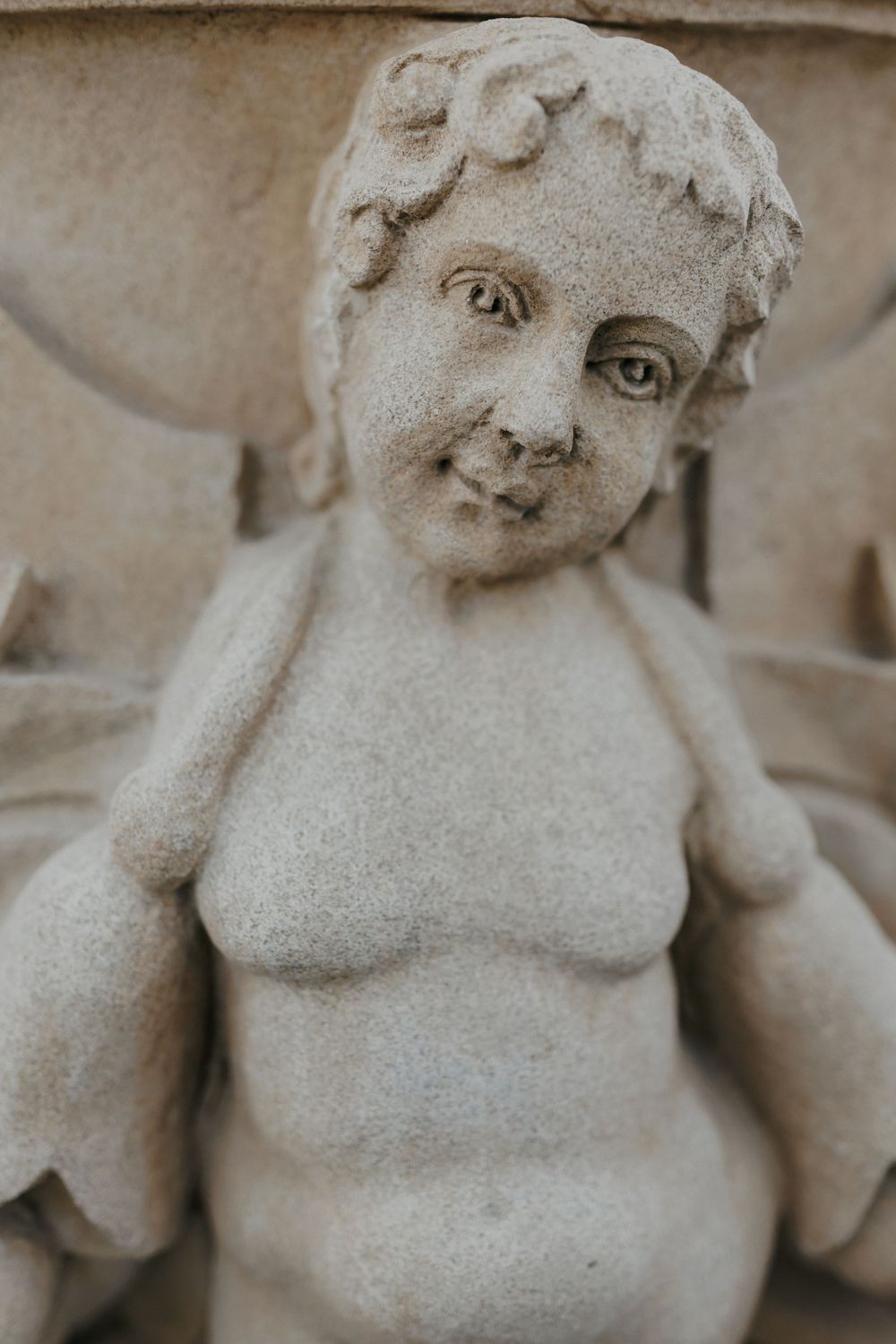 Close-up of cherub stone statue with weathered patina texture.