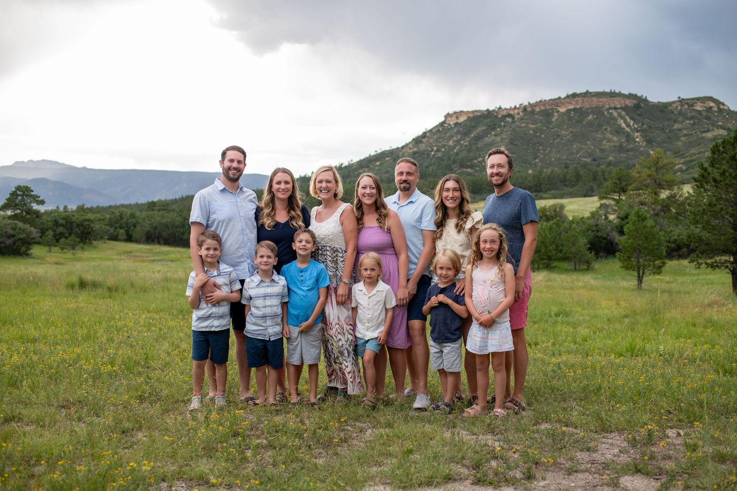 A large group poses for a family portrait in a mountain meadow on a cloudy day.