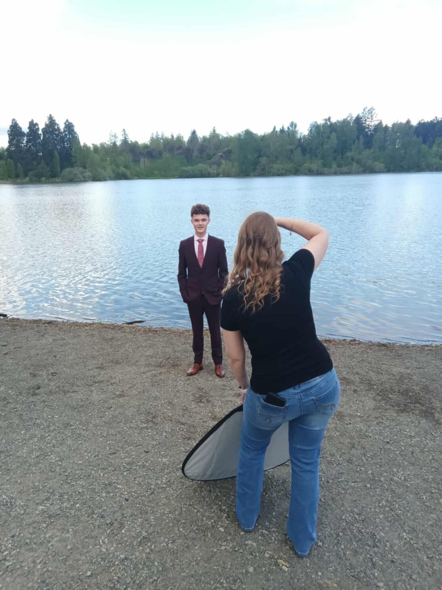 Behind the scenes of a photoshoot by a lake with photographer capturing subject in formal wear.