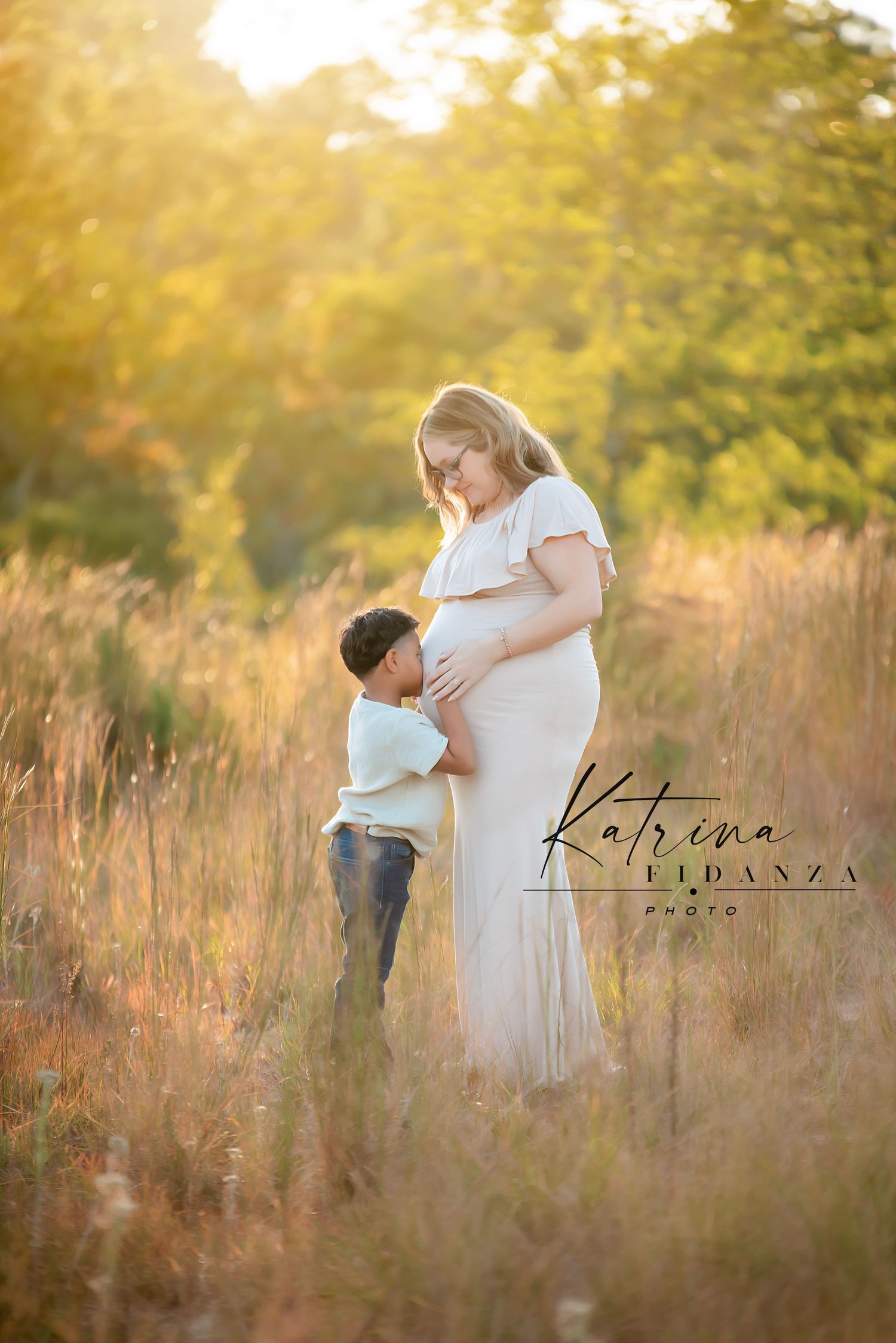 Maternity photo of mother and child in golden field at sunset.
