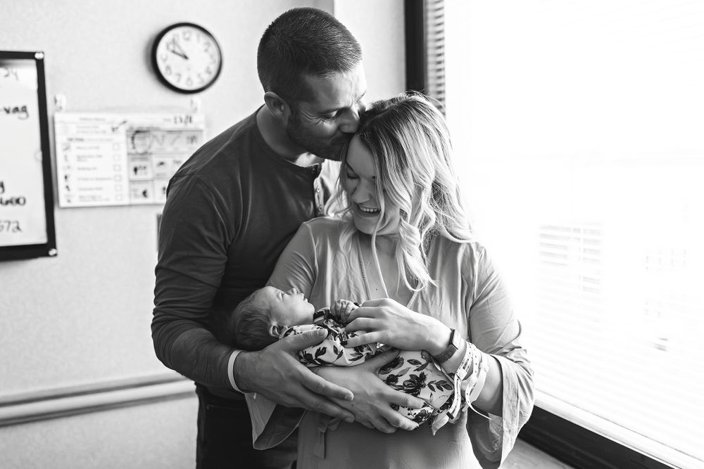 A couple stands in a hospital room at St.John in Tulsa,OK holding their newborn baby in a tender black and white moment.