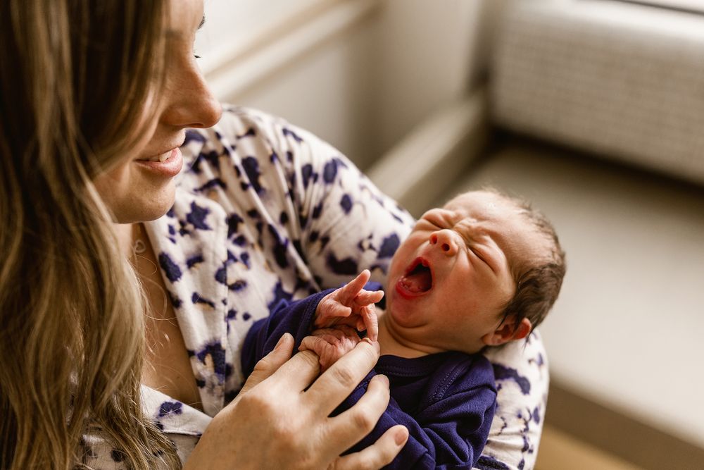 Mom holding her newborn son while he yawns at their fresh 48 session