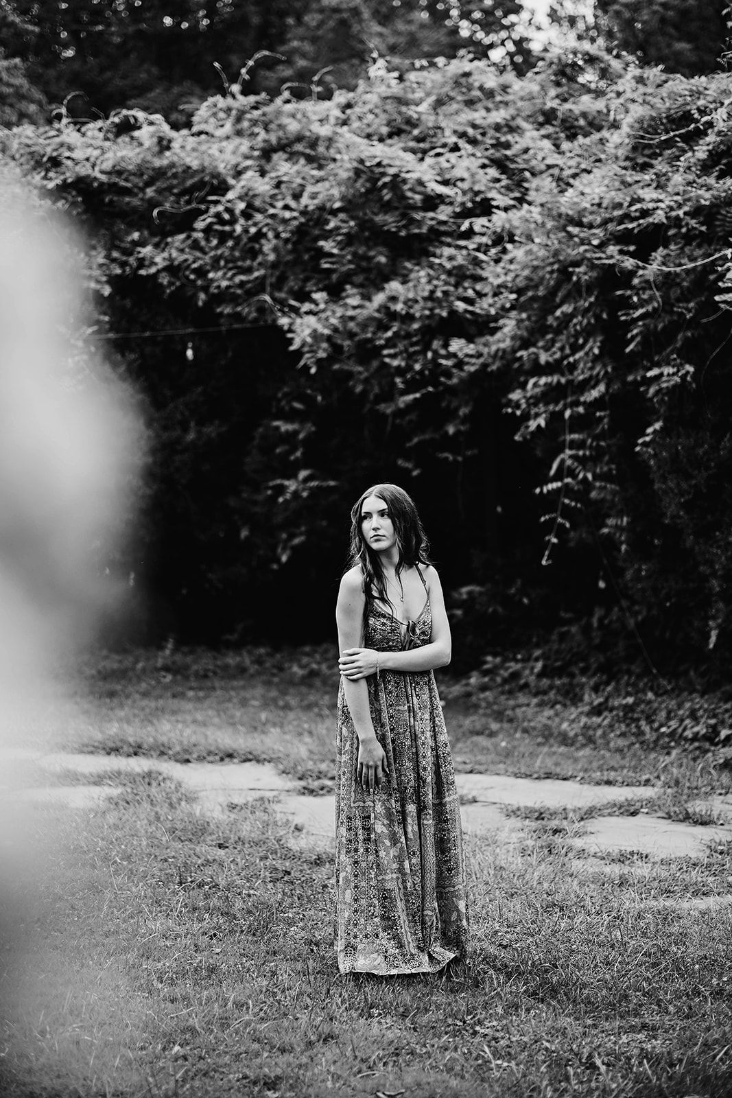 A black and white artistic portrait of a woman in a floral dress sitting in an outdoor setting, near Lancaster County PA