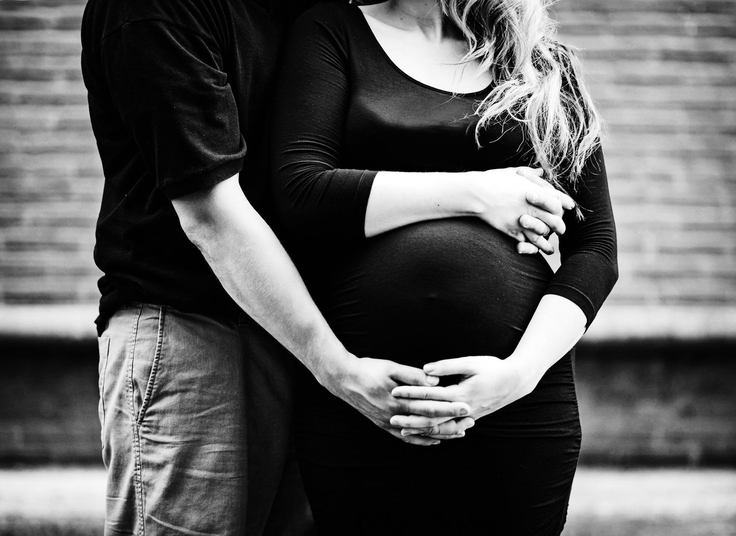 A black and white maternity photo showing a pregnant belly with hands tenderly placed on it in the city near Harrisburg PA in Dauphin County