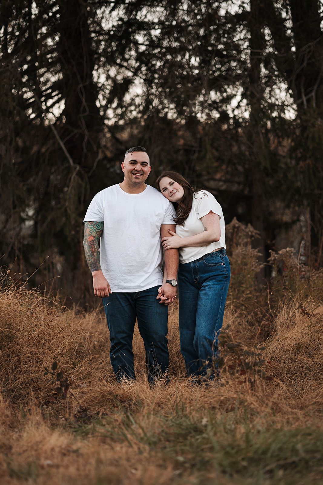 A photograph of a couple that stands together in an outdoor setting with tall grass and trees, excited to announce their engagement. York PA