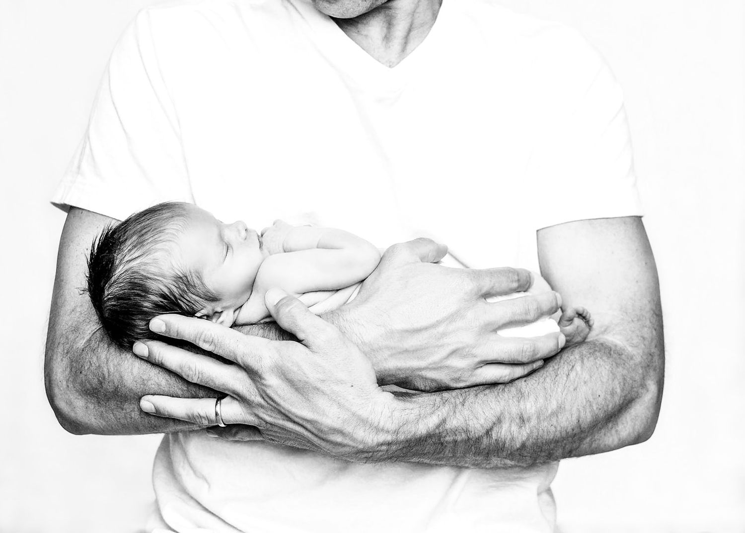 Black and white portrait of a newborn baby in dad's arms on a classic white background near Millerburg PA in Dauphin County PA.