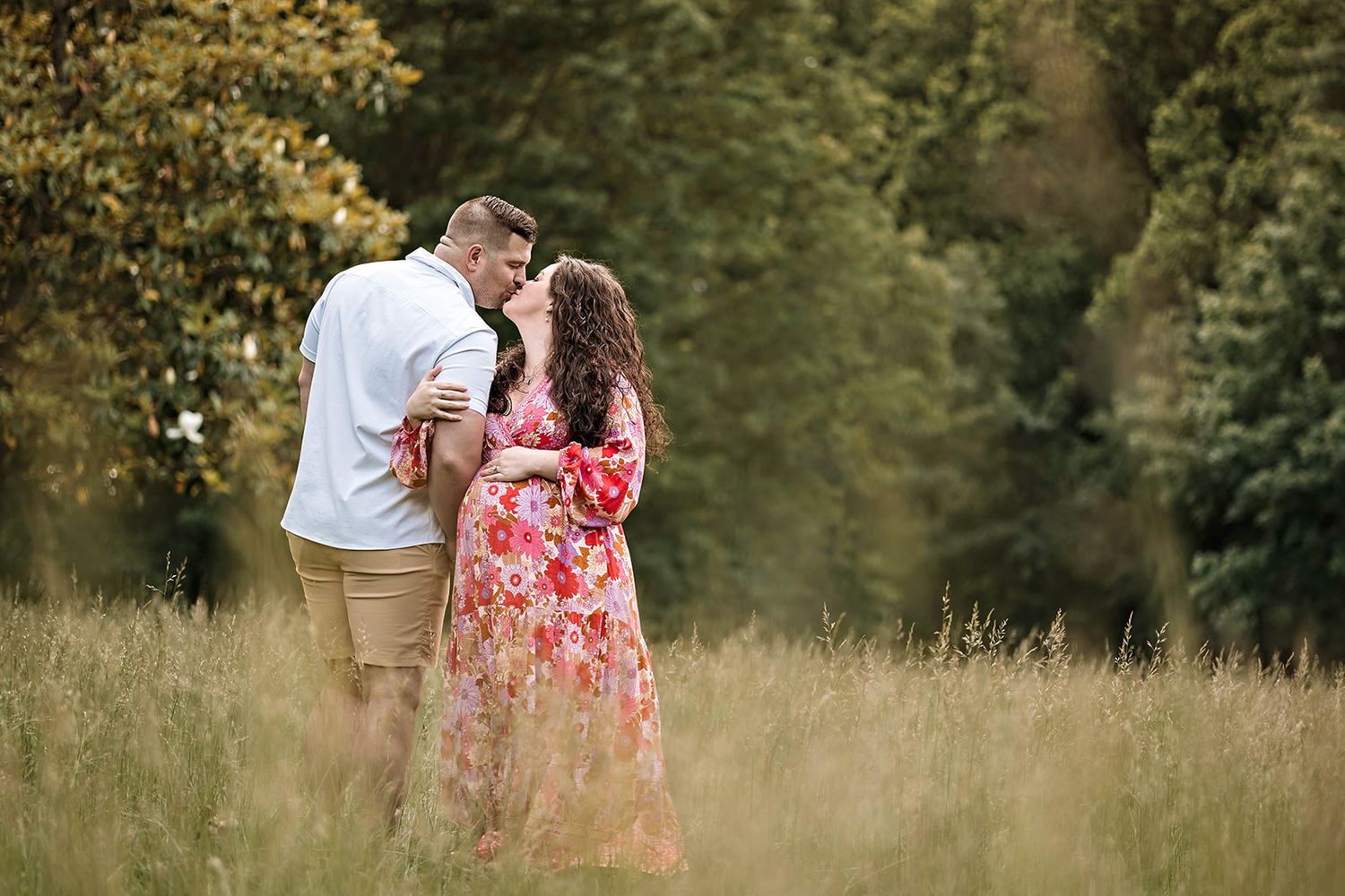 A portrait of a couple expecting a baby in a sun-drenched meadow with tall grass and trees in a romantic maternity session in Dauphin County