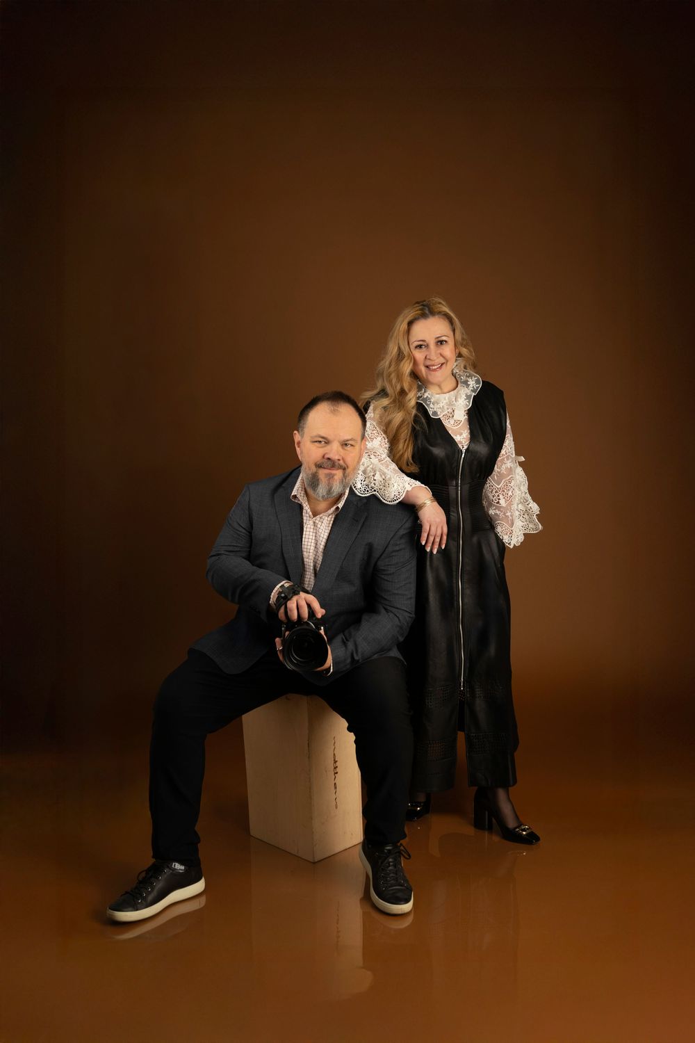 Professional studio portraits showing casual poses with a wooden box against a dark brown backdrop.
