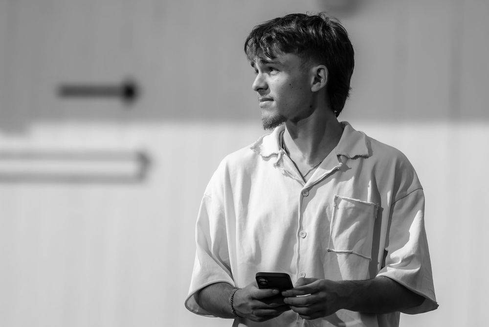 Black and white portrait of a person wearing a white polo shirt holding a phone and looking to the side.